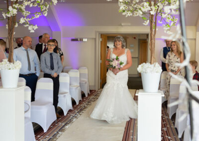 bride walking down the aisle surrounded by flowers and guests