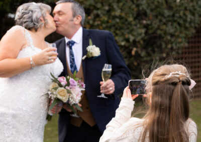 bride and groom kiss as a little girl takes their photograph