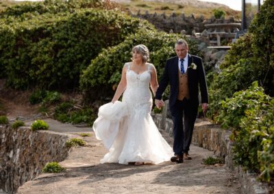 bride and groom strolling along the wall by the beach surrounded by green foliage