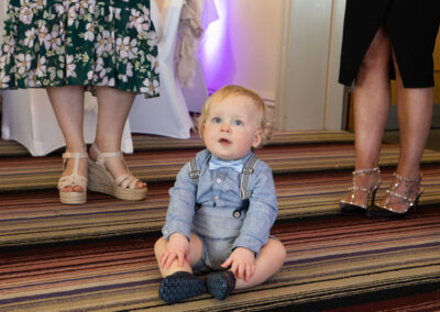 baby boy sitting on the carpet with a pair of women's legs either side of him