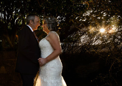 bride and groom facing one another with the sun shining in the background