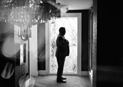 groom in silhouette checking his reflection in a mirror, chandelier in the foreground by Anglesey wedding photographer Gill Jones Photography