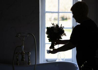 silhouette of bridesmaid drying the stems of a bouquet by Anglesey wedding photographer Gill Jones Photography