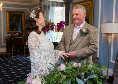 groom placing ring on to bride's finger smiling at one another by Anglesey wedding photographer Gill Jones Photography