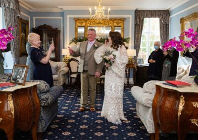 bride blows a kiss towards her family who are watching ceremony on a mobile phone by Anglesey wedding photographer Gill Jones Photography