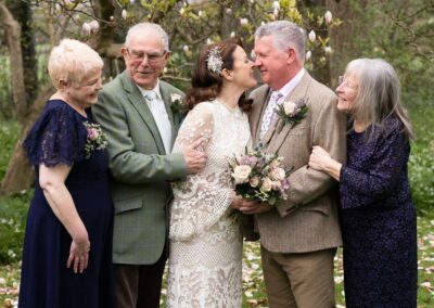 bride and groom almost kissing as family look on by Anglesey wedding photographer Gill Jones Photography