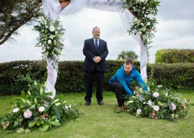 the groom repositions a flower arrangement whilst a guest looks on by anglesey photographer Gill Jones Photography