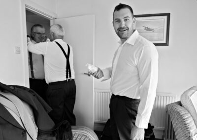 a groom holds a used nappy with an astonished expression whilst two men adjust their ties in the background by Anglesey photographer Gill Jones Photography