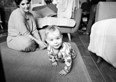 a baby crawls forwards with very wide eyes her mother looks on in the background by Anglesey photographer Gill Jones Photography
