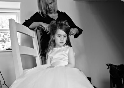 a little girl looks mesmerised as a hairdresser styles her hair by Anglesey photographer Gill Jones Photography
