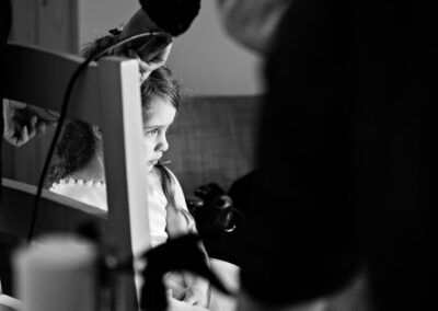 a little girl looks mesmerised as a hairdresser styles her hair by Anglesey photographer Gill Jones Photography