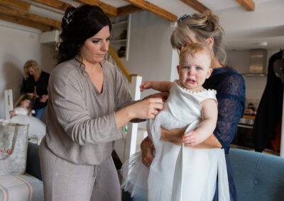 a mother adjusts her baby daughter's dress but the baby is crying by Anglesey photographer Gill Jones Photography