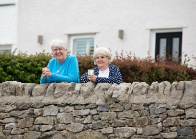 two neighbours lean on a wall and watch the wedding in the garden by Anglesey photographer Gill Jones Photography