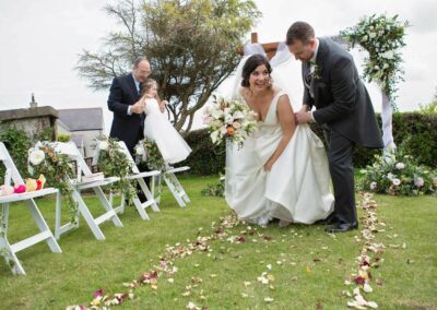 the bride picks the hem of her dress up as she walks with her groom by Anglesey photographer Gill Jones Photography