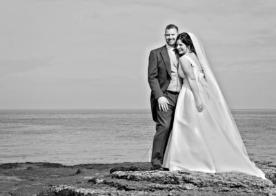 the bride and groom snuggle up as they stand on the rocks by Anglesey photographer Gill Jones Photography