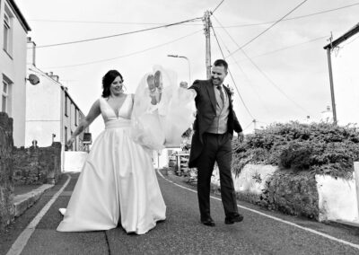 a bride and groom walk down the road and swing their daughter by her hands, we can just see the girl's feet and skirts by Anglesey photographer Gill Jones Photography