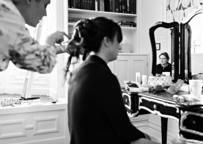 bride having her long hair styled in foreground while young girl's reflection is visible in a mirror by Anglesey wedding photographer Gill Jones Photography