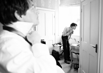 groom tying his tie in the foreground as his son adjusts his tie in a mirror in the background by Anglesey wedding photographer Gill Jones Photography