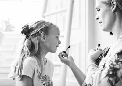 woman takes a mascara brush towards a very young bridesmaid by Anglesey wedding photographer Gill Jones Photography