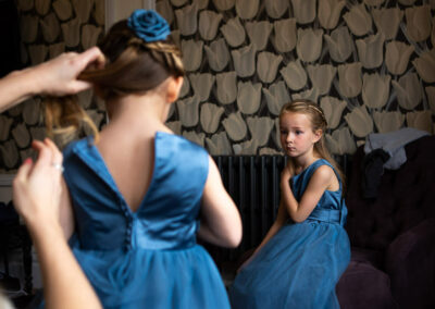 young bridesmaid looks on as another bridesmaid has her dress buttoned up by Anglesey wedding photographer Gill Jones Photography