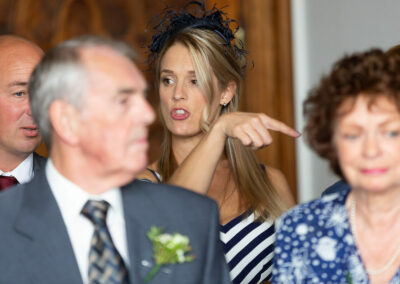 friend sitting amongst guests points to suggest someone should move seats by Anglesey wedding photographer Gill Jones Photography