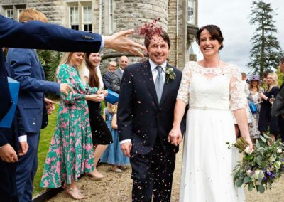 a hand reaches towards the bride and groom and throws confetti towards them by Anglesey wedding photographer Gill Jones Photography