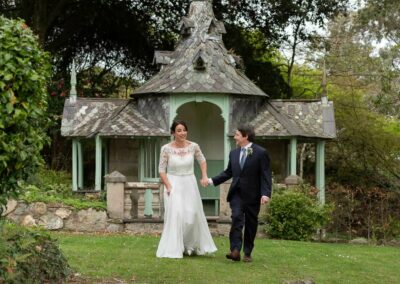 bride and groom hand in hand about to break into a run with a summer house in the background by Anglesey wedding photographer Gill Jones Photography Anglesey wedding photographer Gill Jones Photography