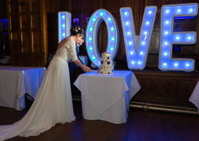 bride and groom cutting their wedding cake, a huge Love sign in behind them by Anglesey wedding photographer Gill Jones Photography