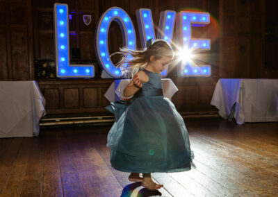 little bridesmaid twirling the skirts of her dress with the word love behind her by Anglesey wedding photographer Gill Jones Photography