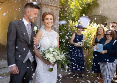 bride and groom smiling as confetti flutters by by Anglesey photographer Gill Jones