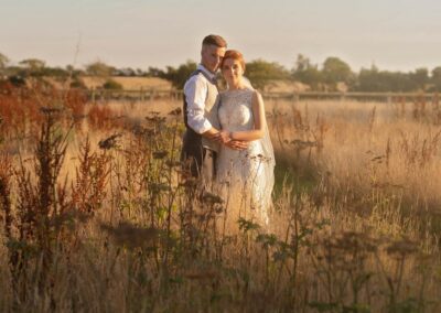 bride and groom embracing whilst standing in a field of golden grasses by Anglesey photographer Gill Jones