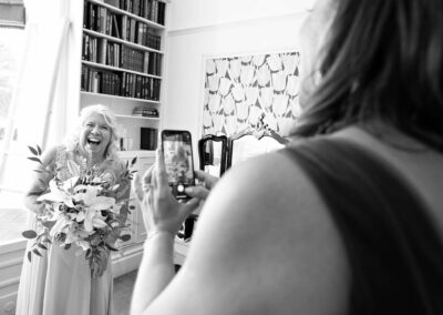 bride laughing as her friend takes her photograph by Anglesey photographer Gill Jones