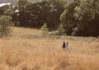 bride and groom walking through a field of golden long grass by Anglesey wedding photographer Gill Jones