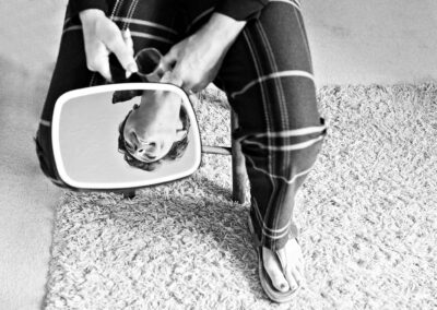 woman sitting on a stool holding a mirror so her smile is visible in the mirror only by Anglesey wedding photographer Gill Jones