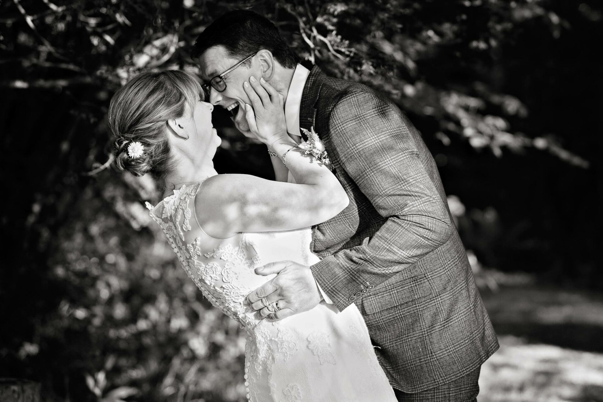 couple facing eachother she has her partner's face in her hands and they're laughing by Anglesey wedding photographer Gill Jones