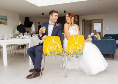 bride and groom look towards each other whilst sitting on bright yellow chairs by Anglesey wedding photographer Gill Jones