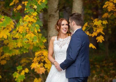 Bright yellow and green foliage surrounds a bride as she looks into her groom's eyes by Anglesey wedding photographer Gill Jones
