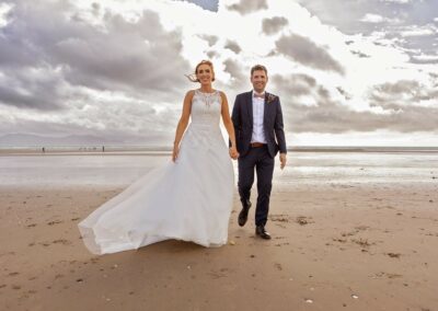 bride and groom walking hand in hand with the sea and mountains in the background by Anglesey wedding photographer Gill Jones