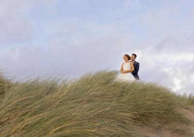 bride and groom standing in the dunes embrace whilst looking towards the horizon by Anglesey wedding photographer Gill Jones