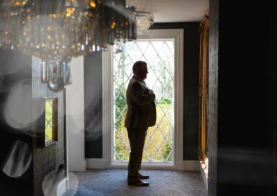 silhouette of a groom against a full length mirror with a chandelier in the foreground by Anglesey wedding photographer Gill Jones
