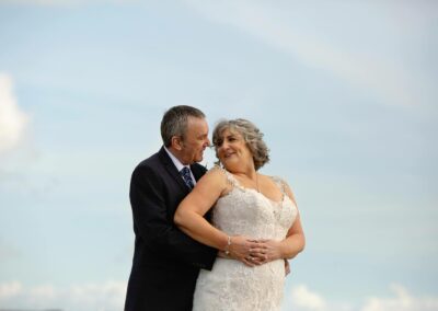 bride and groom caressing with a blue sky in the background by Anglesey wedding photographer Gill Jones