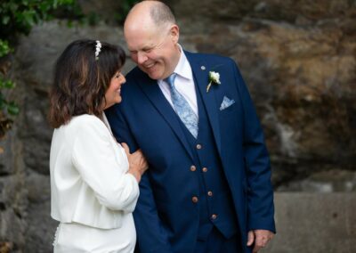 couple looking towards each other and laughing as the bride squeezes the groom's arm by Anglesey wedding photographer Gill Jones