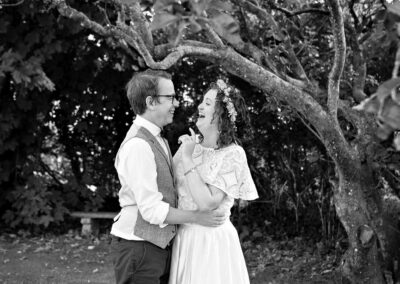 bride and groom laughing beneath a big tree by Anglesey wedding photographer Gill Jones