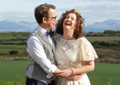 bride and groom embracing and laughing with a mountain range in the background by Anglesey wedding photographer Gill Jones