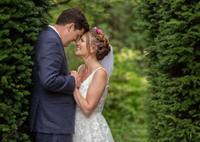 bride and groom giggling whilst clutching each other amongst the pine trees at Chateau Rhianfa by Anglesey wedding photographer Gill Jones