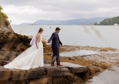 groom leading bride down a stone jetty towards the sea by Anglesey wedding photographer Gill Jones