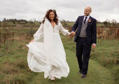 bride and groom walking hand in hand ina field with the wind blowing at her dress