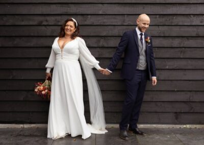 Bride and groom hand in hand against a black featherboard building by Anglesey wedding photographer Gill Jones