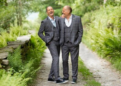 groom and groom laughing surrounded by bright green ferns by Anglesey wedding photographer Gill Jones