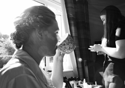 bride drinking from a cup whilst having her makeup applied by Anglesey wedding photographer Gill Jones